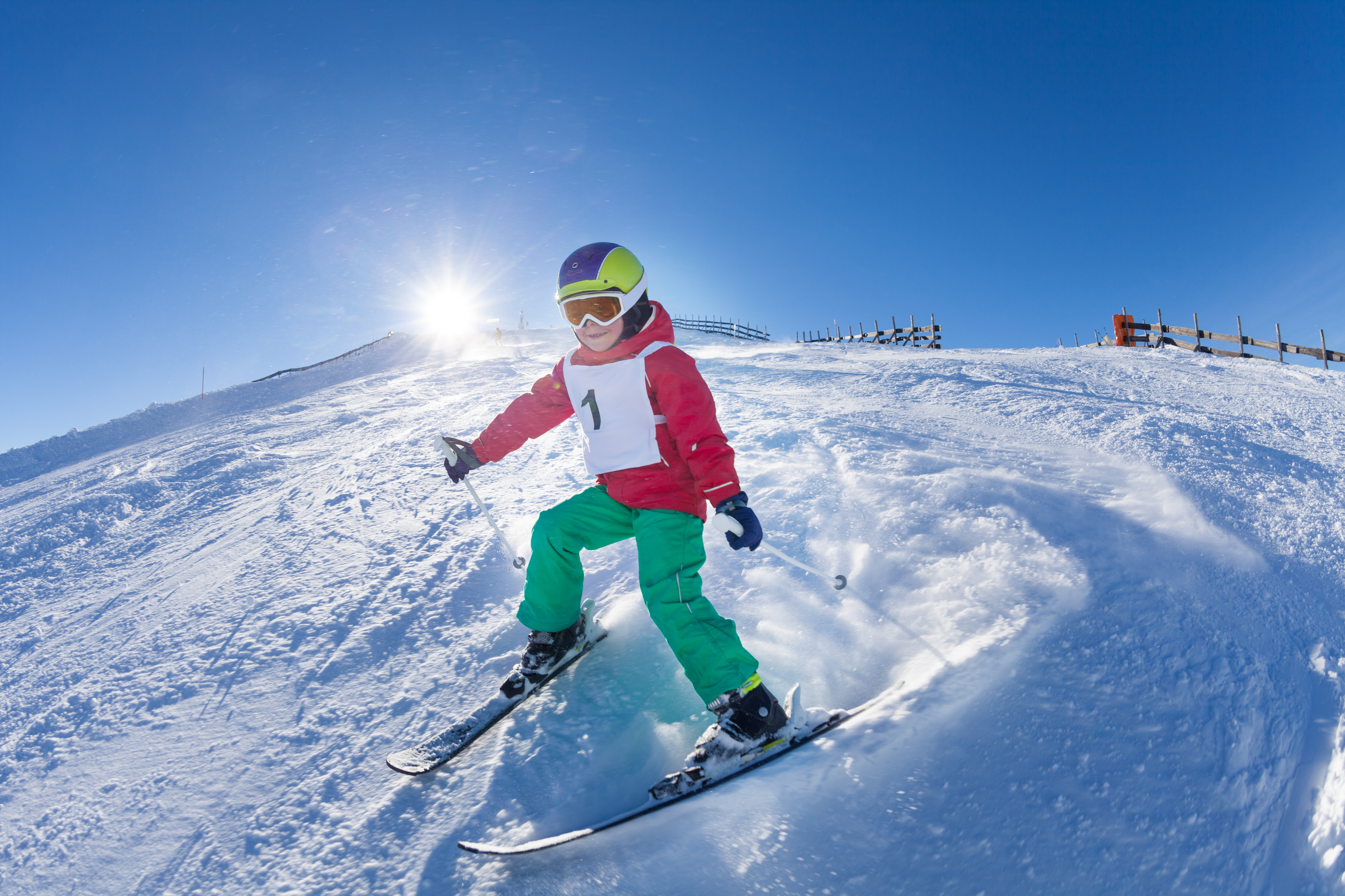 Active kid boy with safety helmet, goggles and poles skiing in mountains at sunny day