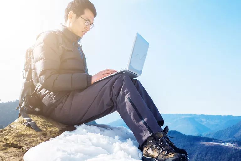 man sits on top on of mountain using laptop