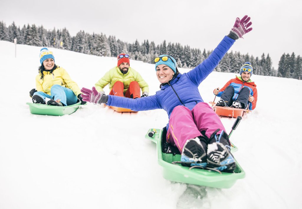 group of friends in bright winter clothing enjoy sledging down a snowy hill