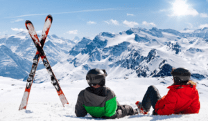 Two skiers sitting on the top of the mountain enjoying the view.